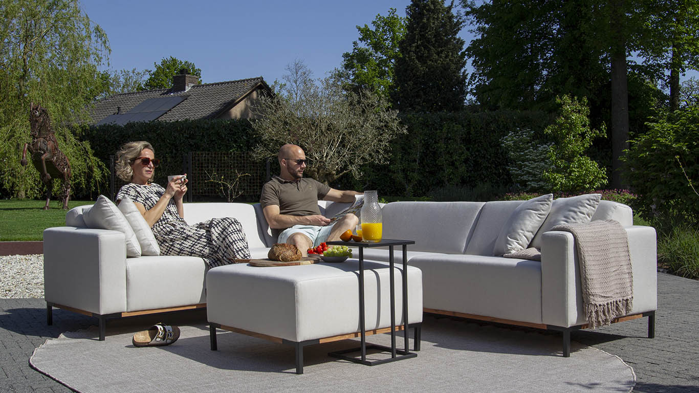 Genieten in de tuin van je UrbanSofa Outdoor stoffen tuinbank Marbella in een Hoekbank opstelling in de stof Sunbrella Natte met bijpassende Marbella Hocker