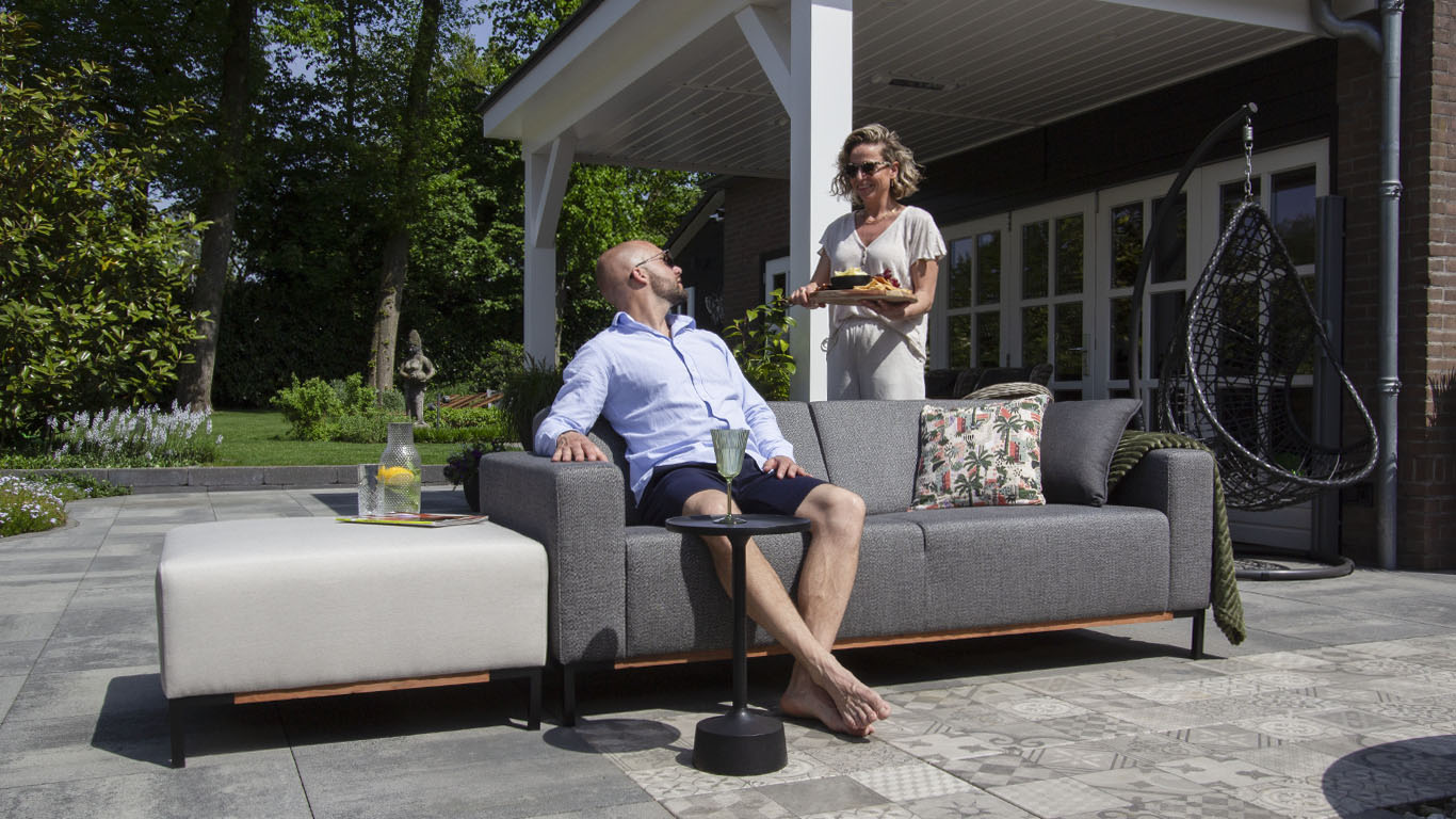 Samen genieten in de tuin met een UrbanSofa Outdoor stoffen tuinbank Marbella Sofa in Sunbrella Savana Tornado, gecombineerd met Marbella hocker.