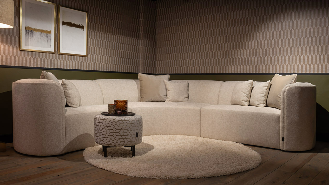 Moderne UrbanSofa Louise Hoekbank met ronde vormen in de stof Rio Sand met Paris Hocker in Fairmont Shiny Desert.